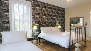 Ein Hotelzimmer mit zwei Betten, einem großen Fenster mit Jalousien, Stadtlandschafts-Tapete, einem Chandelier und einem Spiegel an der Wand.
