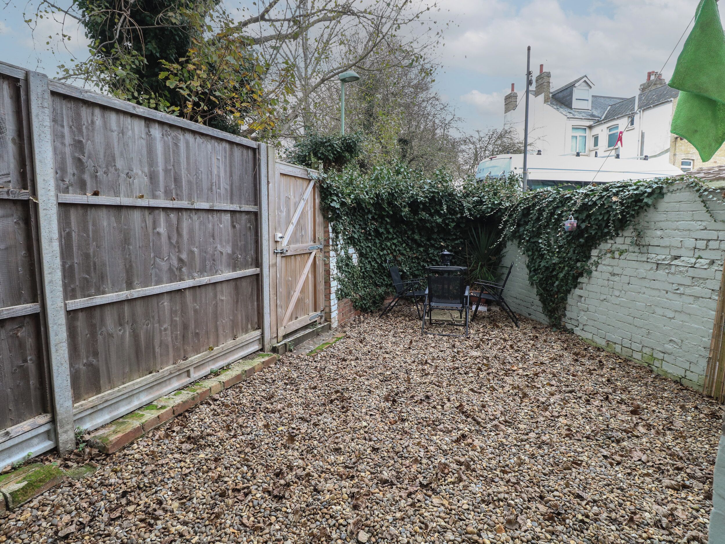 A backyard with a wooden fence, a table with chairs, and a white wall covered in ivy.