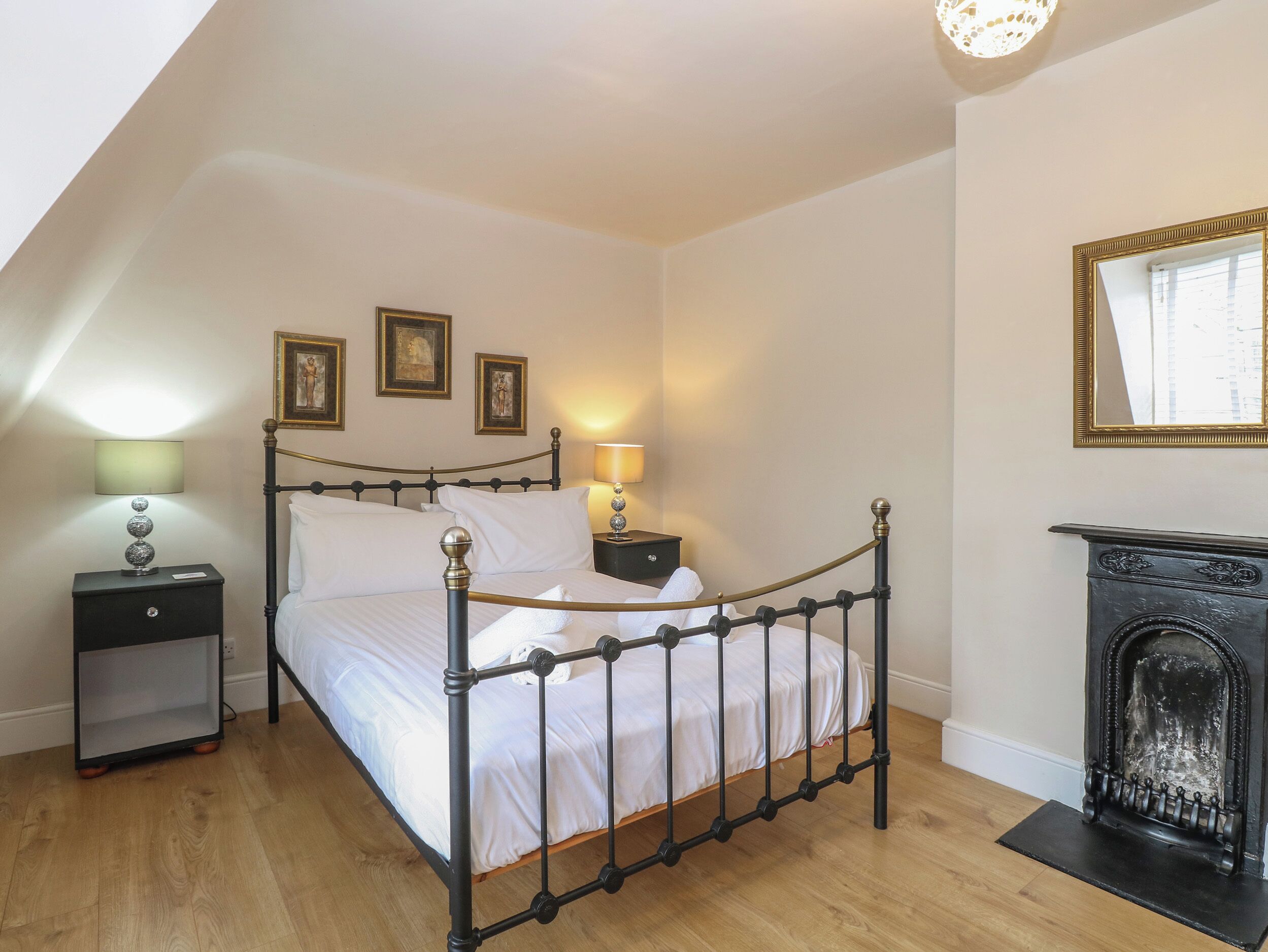 A bedroom with a four-poster bed, two bedside tables, a mirror, and a fireplace.