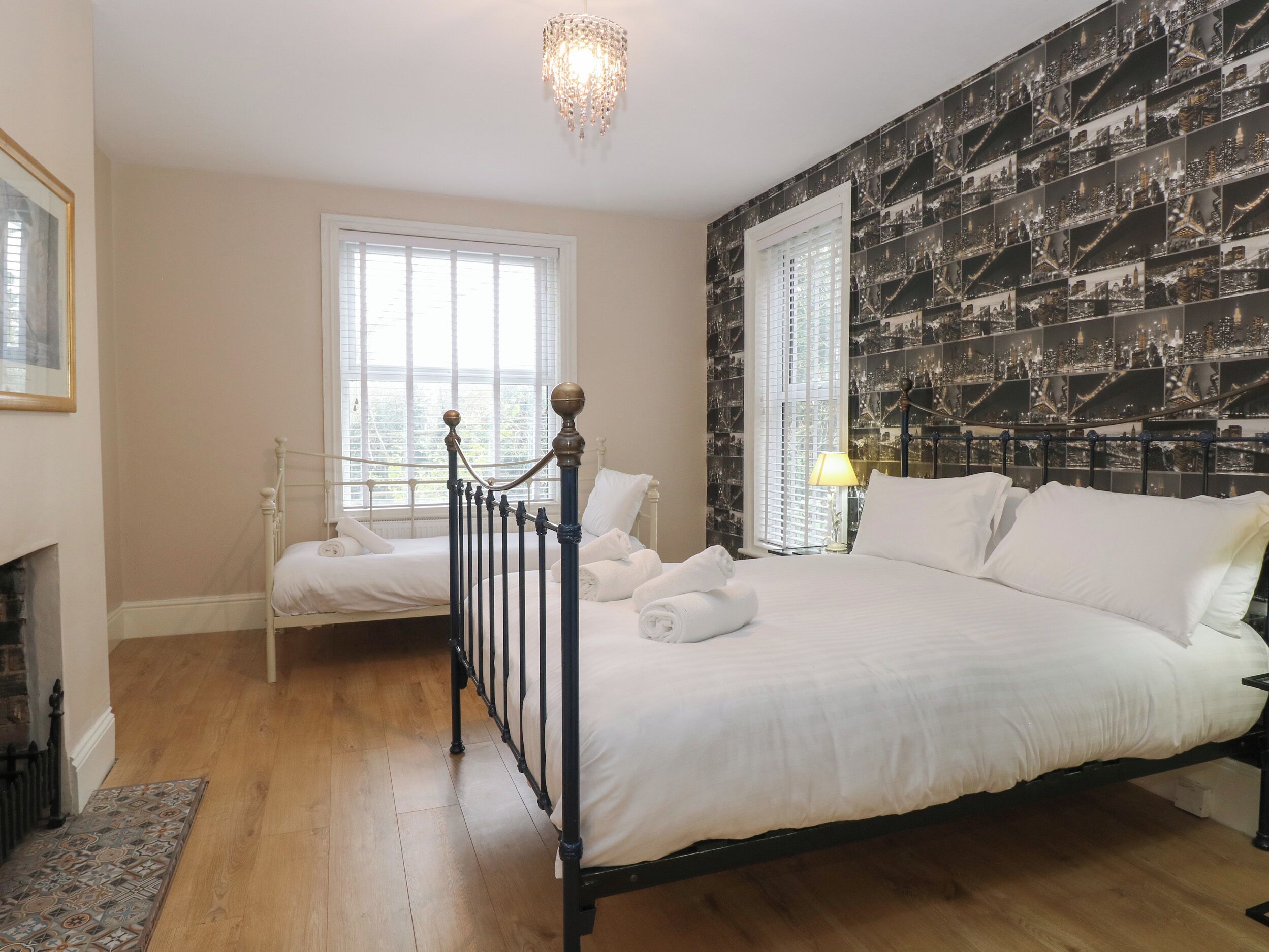 A bedroom with a large bed, two windows, a chandelier, and a cityscape wallpaper.