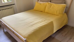 A bed with a yellow bedspread and pillows, a wooden headboard, and a radiator in the background. - LAKE AND MOUNTAIN (Civenna)