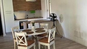 A modern kitchen with wooden cabinets, a white refrigerator, and a dining area with a round table and chairs. - LAKE AND MOUNTAIN (Civenna)
