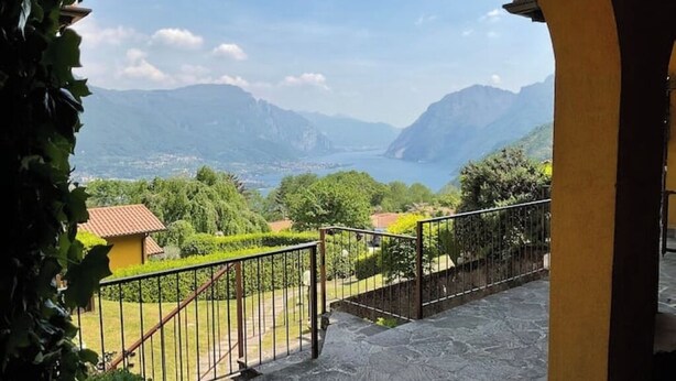 A stone staircase leading to a balcony with a metal railing, overlooking a mountainous landscape and a body of water. - LAKE AND MOUNTAIN (Civenna)