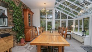 Un espace repas avec une table et des chaises en bois, un mur en pierre agrémenté de plantes, un meuble en bois et une grande baie vitrée.
