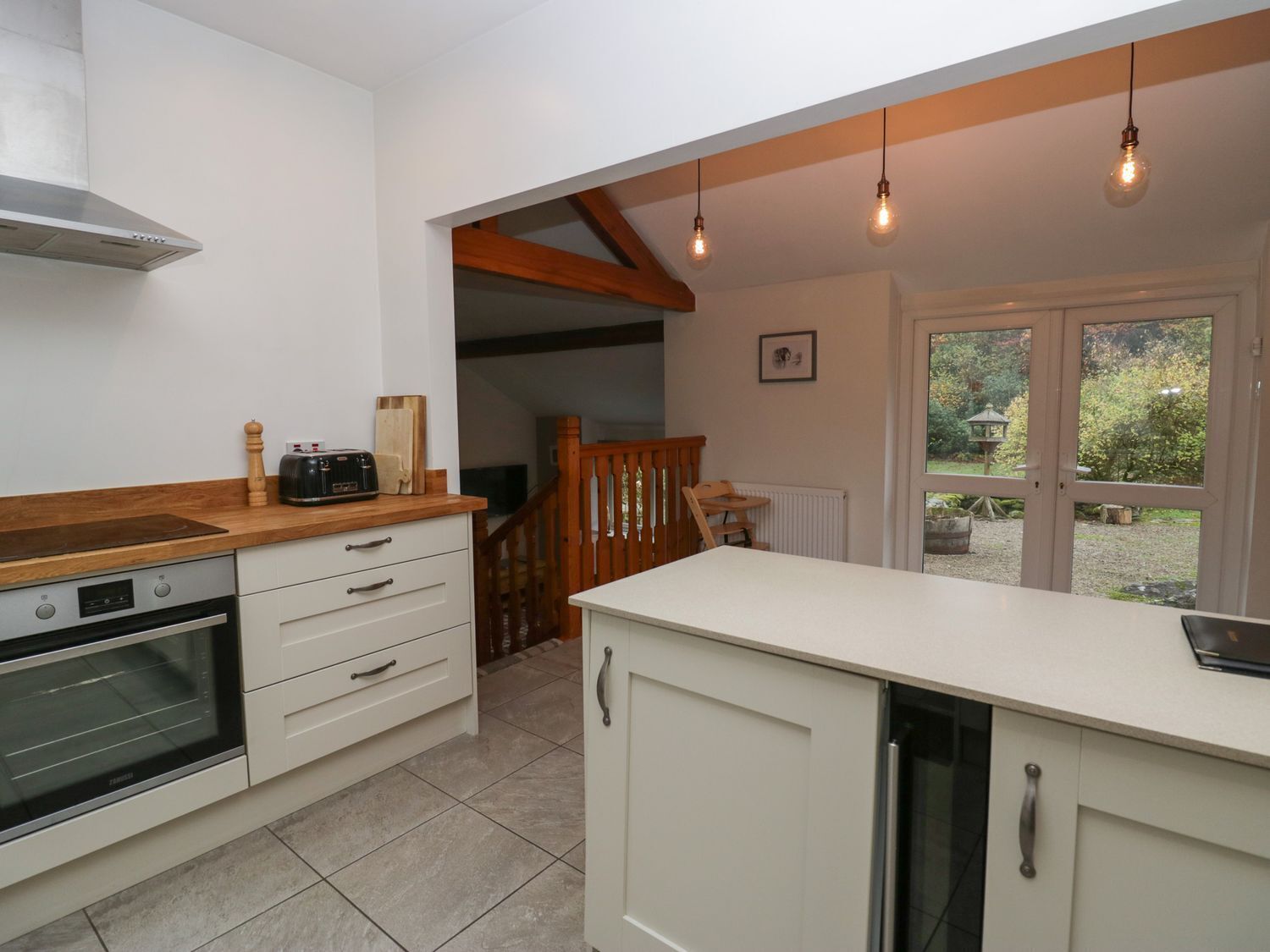 A kitchen with white cabinets, a wooden countertop, and a built-in oven. There is a window with a view of greenery outside.