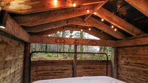 Une cabane en bois dotée d’un bain à remous, de poutres apparentes et de guirlandes lumineuses.