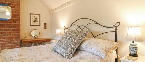 Quarto com cama, mesa de cabeceira, abajur, espelho e um quadro na parede.