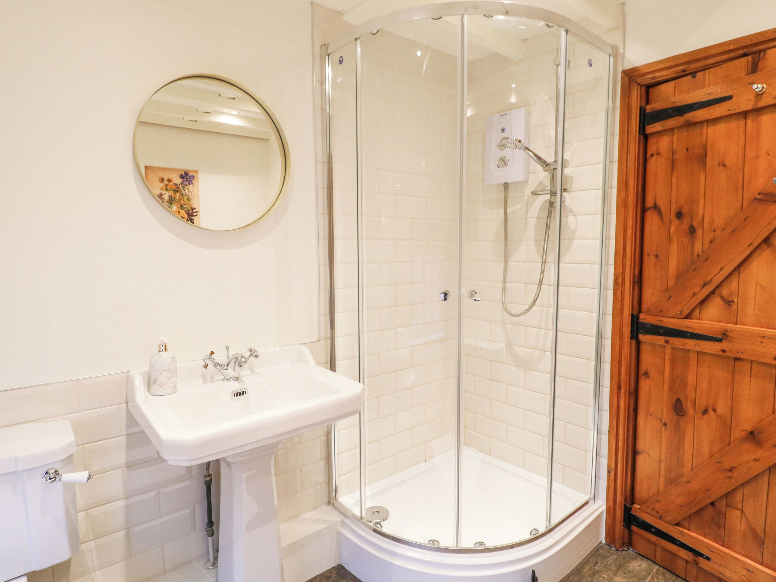 Un bagno con doccia vetro, lavandino bianco e porta in legno.