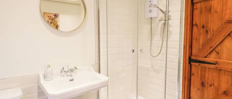 A bathroom with a glass-enclosed shower, a white sink, and a wooden door.