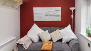 Un divano grigio con quattro cuscini, un tavolino di legno e un quadro raffigurante una scena costiera.
