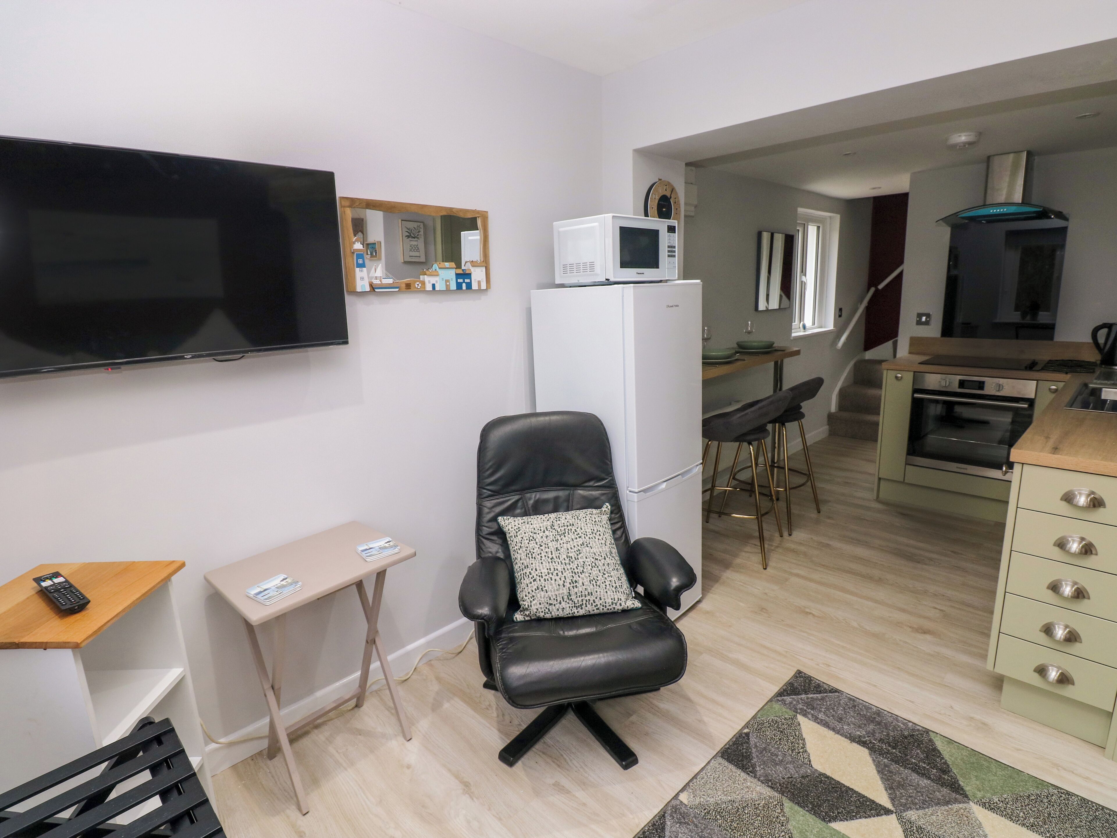 Un espace de vie compact comprenant un téléviseur à écran plat, une petite kitchenette, un coin repas avec une table et des chaises, et un coin salon avec un fauteuil et une petite table.