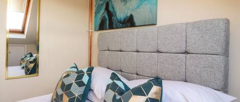 A neatly made bed with patterned pillows, a headboard, a painting on the wall, and a mirror.