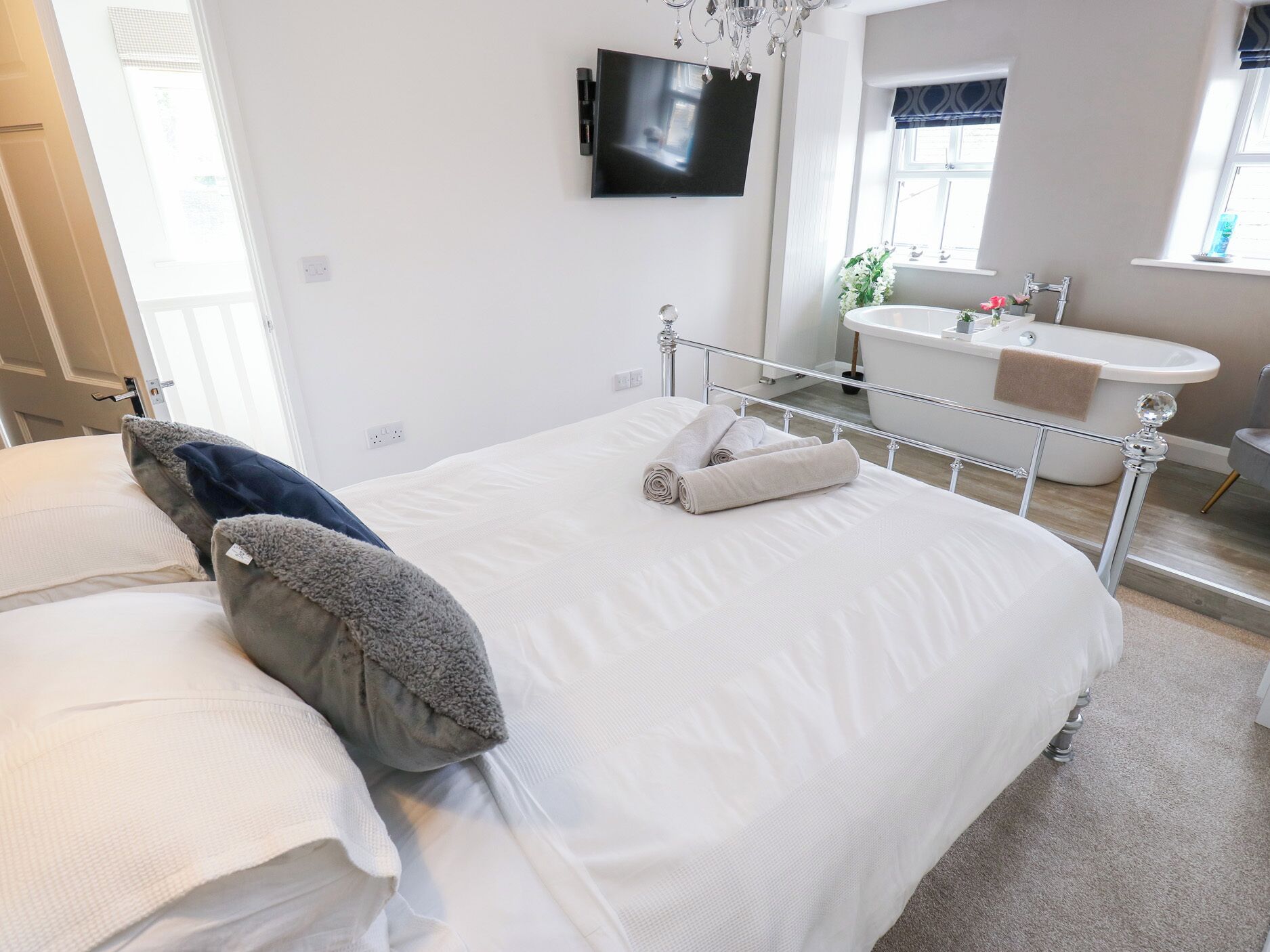 Un dormitorio moderno con una cama grande, un televisor montado en la pared y un baño con bañera y lavamanos.