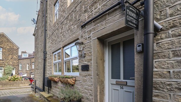 Un edificio de piedra con un cartel que dice 'Welcome to Thimble Cottage, 14 Shirley Street'.