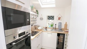 Cocina compacta con horno integrado, microondas y lavavajillas, una pequeña encimera y un tragaluz.