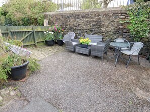 A patio with wicker furniture, a stone wall, and potted plants. - Thimble Cottage (Keighley)