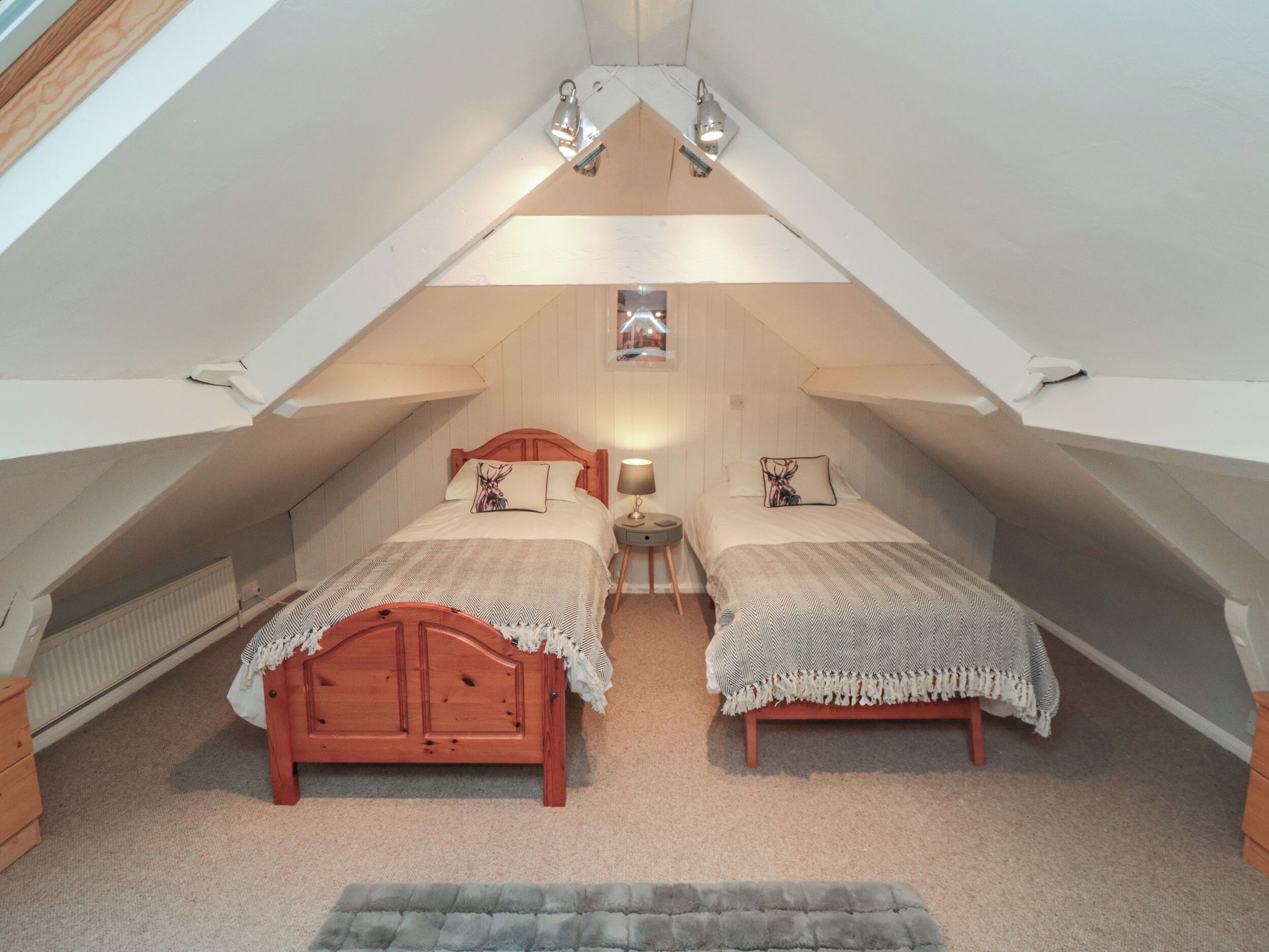 A small, cozy attic bedroom with two wooden beds, a small table, and a radiator.