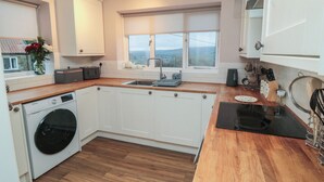 Une cuisine moderne dotée d’un lave-linge encastré, de plans de travail en bois, d’armoires blanches, d’une grande fenêtre offrant une belle vue et d’une plaque de cuisson à induction noire.
