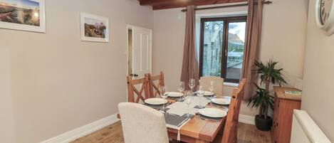 A dining area with a wooden table set for four, wooden chairs, a ceiling light, and a window with curtains.