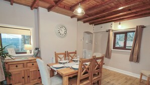 Un coin repas avec une table en bois dressée pour quatre personnes, une horloge au mur et une fenêtre avec des rideaux.