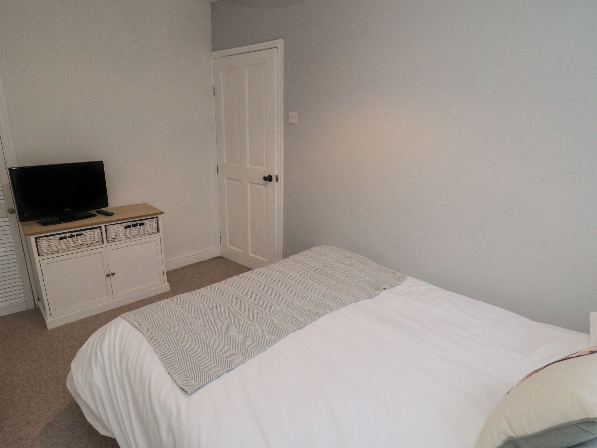 A bedroom with a bed, a television on a dresser, and a door.