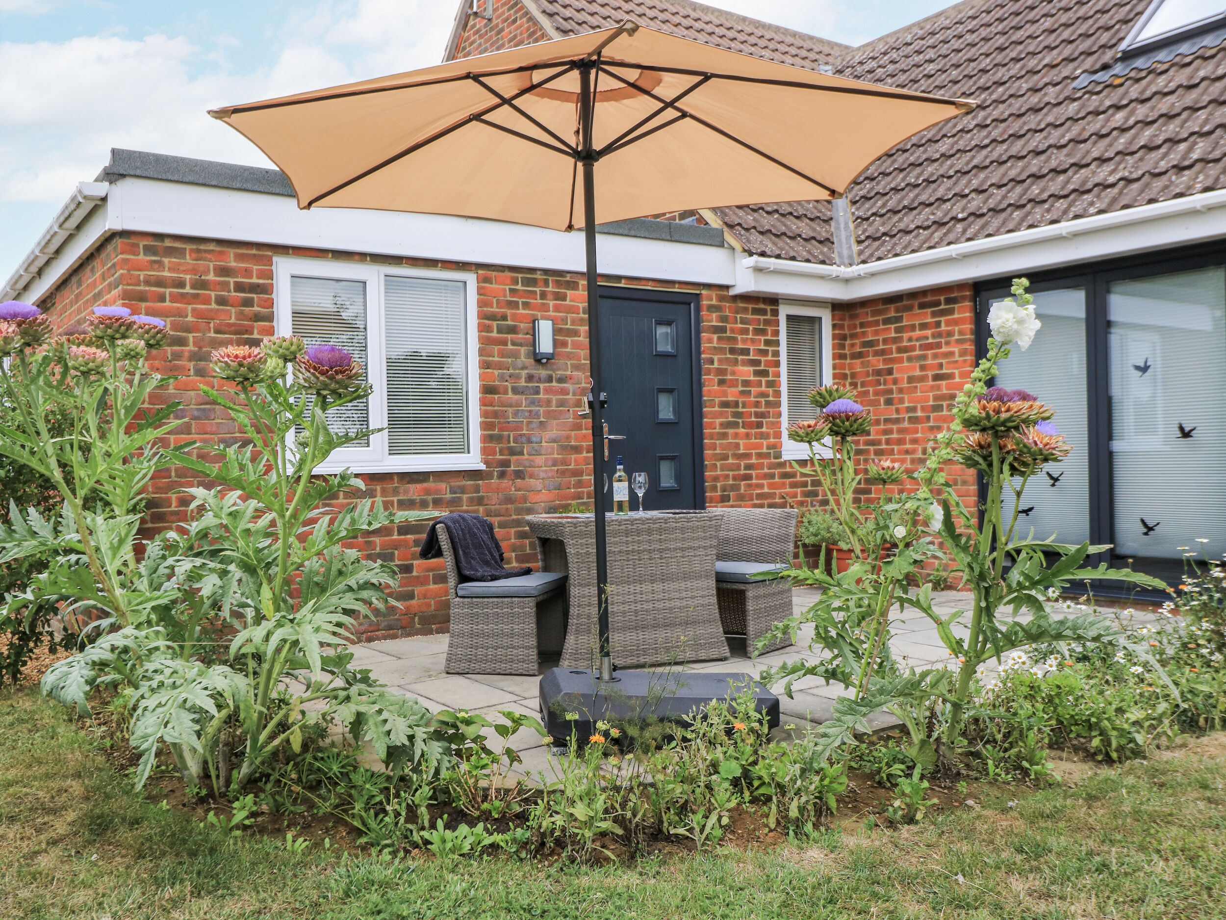 A patio with outdoor furniture, a large umbrella, and a brick house with a dark door.