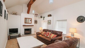 A living room with a fireplace, leather sofas, a TV, and a clock on the wall. - Bayside Cottage (Rosslare)