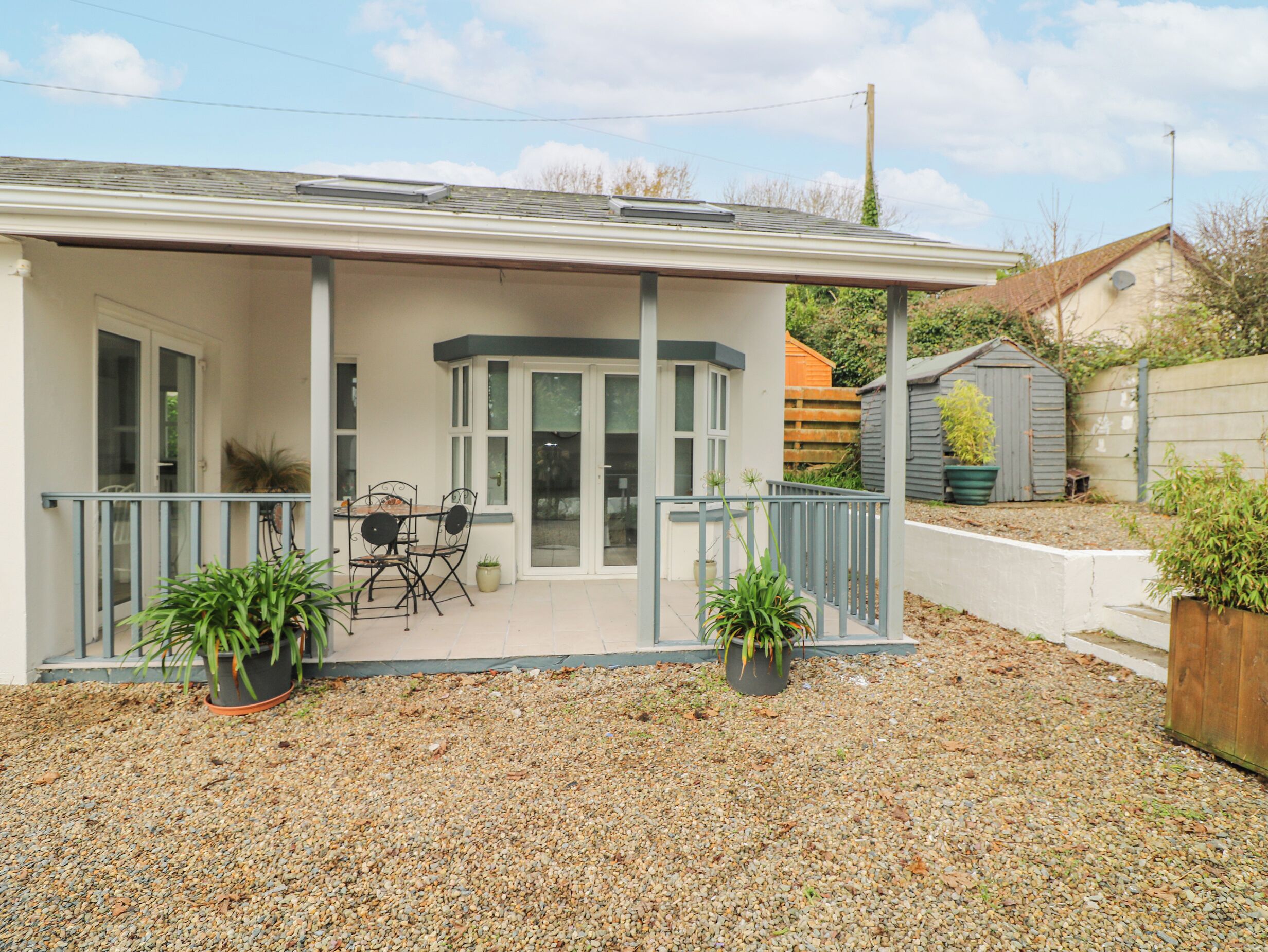 A house with a covered porch, a dining table with chairs, and two potted plants.