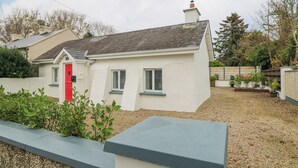 A single-story house with a red door, white exterior walls, and a grey roof. - Bayside Cottage (Rosslare)
