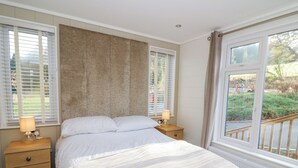 Un dormitorio con una cama grande, dos mesitas de noche con lámparas, un cabecero de madera y vistas al exterior a través de una ventana.