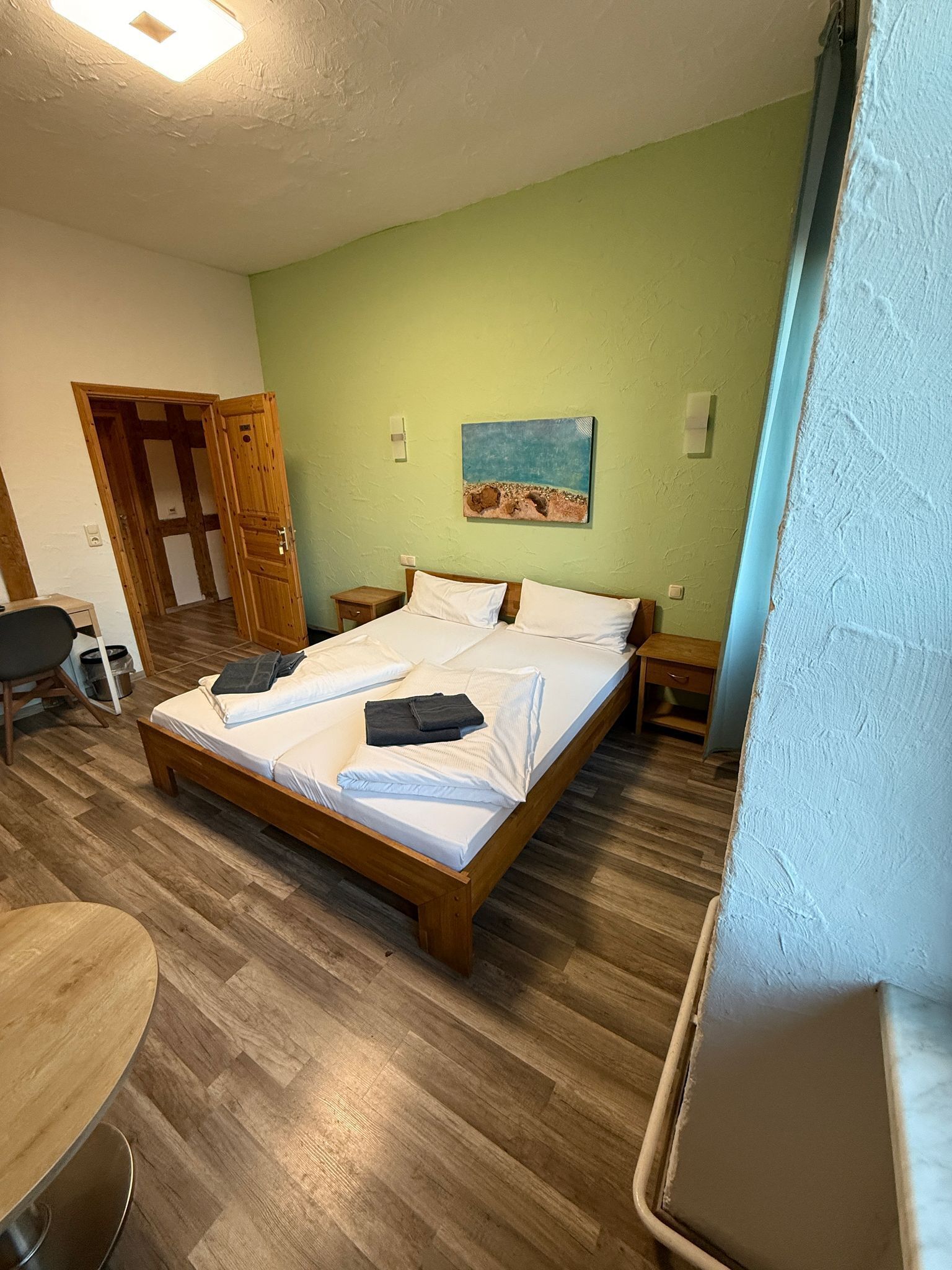 A hotel room with a wooden bed, a desk, a chair, and a painting on the wall.