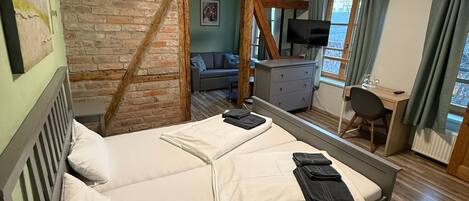 Une chambre avec un lit, un bureau, une chaise, une télévision et une fenêtre avec des rideaux.