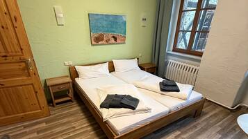 Una stanza con un letto di legno, un comodino, un termosifone e una finestra con tende.