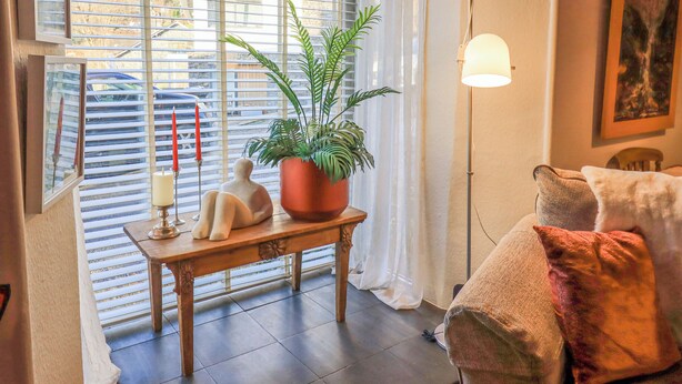 A cozy living room with a wooden table, a potted plant, a floor lamp, and a couch with cushions. - Silverhow Cottage (Ambleside)