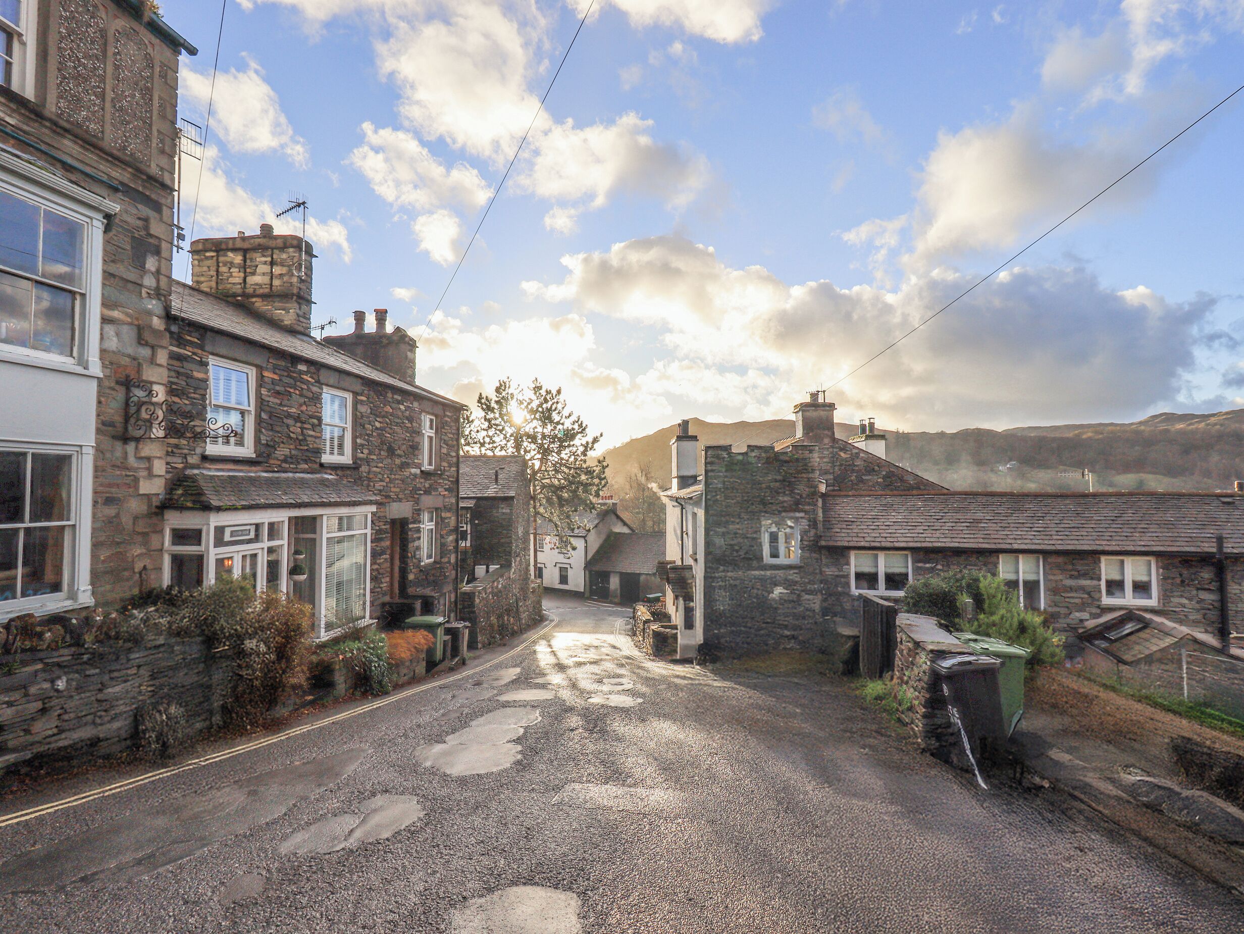 A narrow cobblestone street lined with stone houses, featuring a gravel driveway and a visible drainage system.