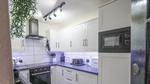 A compact kitchen with white cabinets, a microwave, a toaster, and a stove. - Silverhow Cottage (Ambleside)