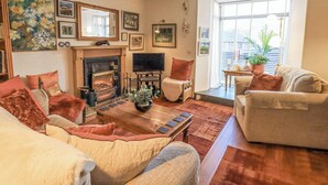 A cozy living room with a fireplace, comfortable seating, and a large window with a view. - Silverhow Cottage (Ambleside)