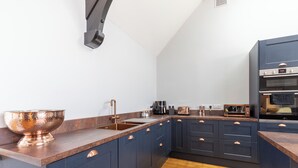 Een moderne keuken met donkerblauwe kastjes, een koperen kom, een spoelbak, een broodrooster en een magnetron.