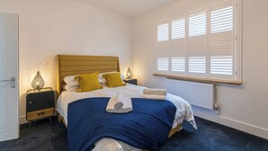 Een slaapkamer met een bed, nachtlampjes, een radiator en een raam met zonwering.