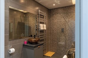 A modern bathroom with a large mirror, a glass-enclosed shower, a wooden tray, and a copper basin on the countertop.