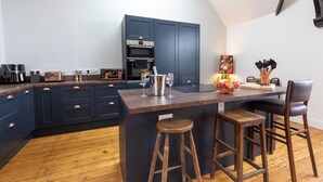 Een moderne keuken met donkerblauwe kastjes, een houten eiland met krukken, een inbouwoven en een decoratieve vaas.