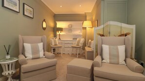 A hotel room with two armchairs, a small table, a lamp, and a view of the kitchen. - Tree Tops (Broadway)