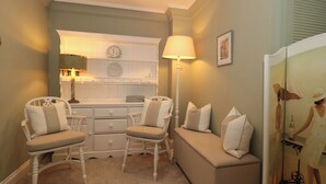 A cozy room with a white vanity, two chairs, a bench, and a floor lamp. - Tree Tops (Broadway)