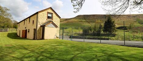 A stone building with a sloped roof, a fenced area, and a grassy field.