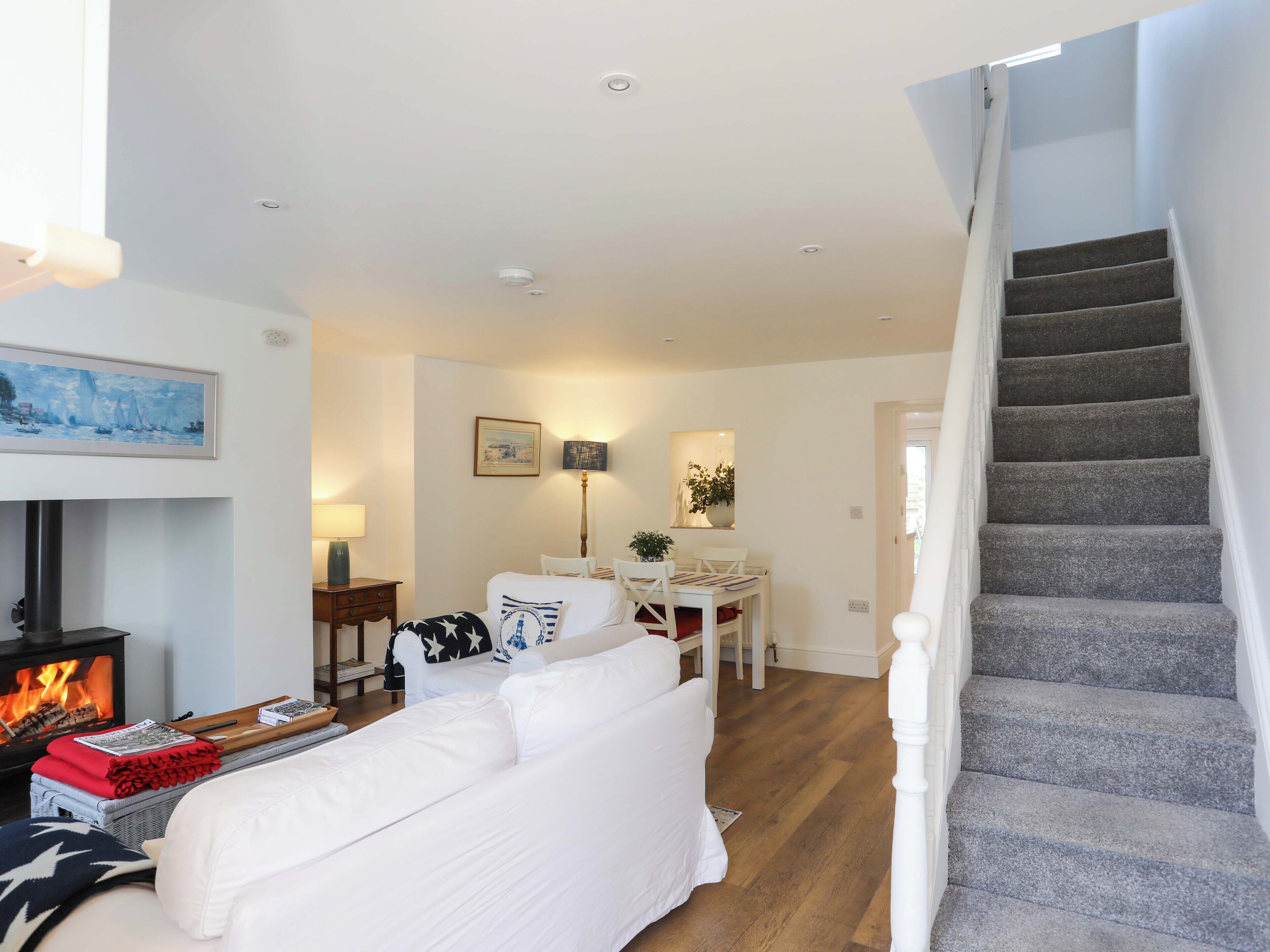 A modern living room with a fireplace, white sofa, dining table, and a staircase.