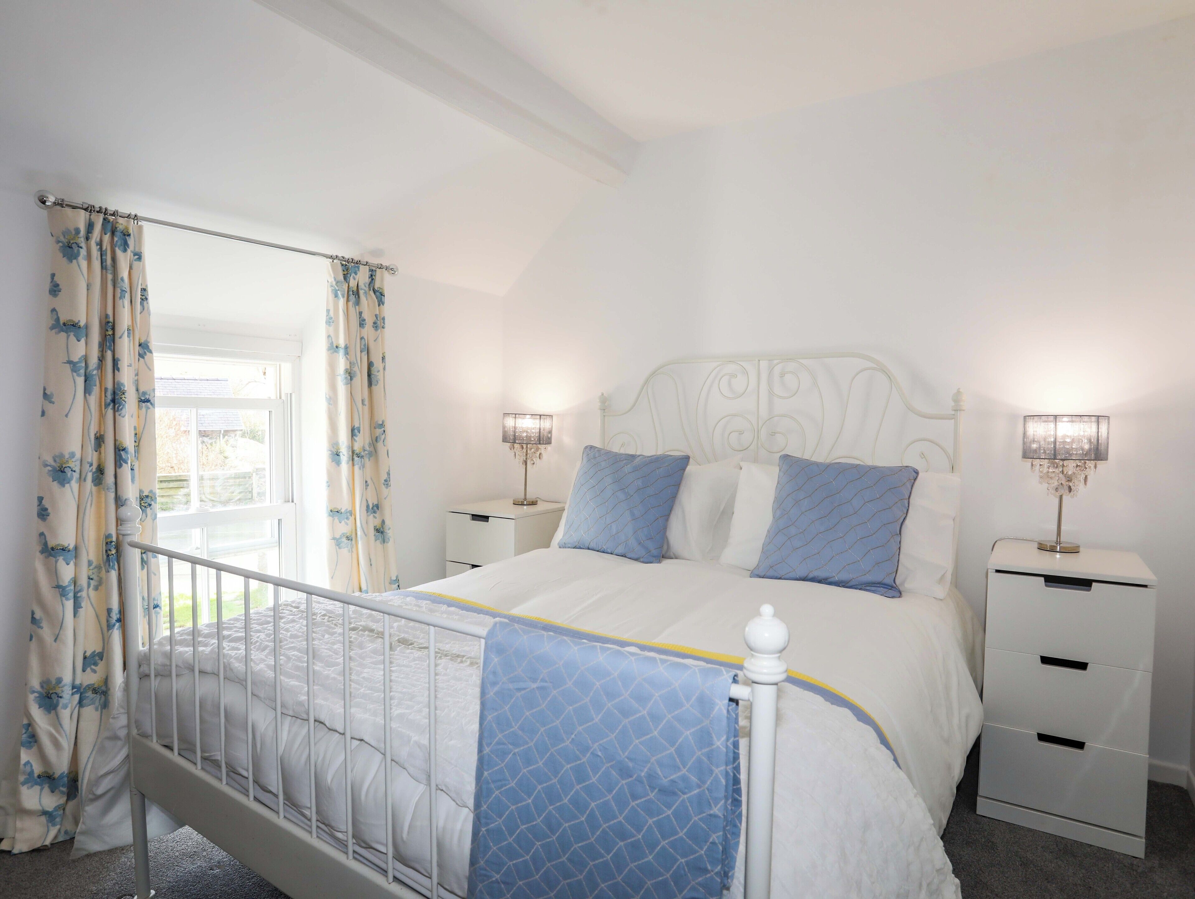 Une chambre à coucher comprenant un lit, deux tables de chevet, une fenêtre avec des rideaux et une petite table de nuit avec une lampe.