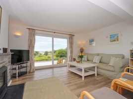 Una sala de estar con chimenea, televisor, sofá, mesa de centro y vistas al exterior.