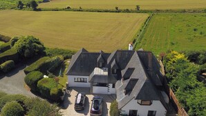 Une maison avec un toit en pente, une allée permettant de garer deux voitures et, au fond, un grand champ verdoyant.