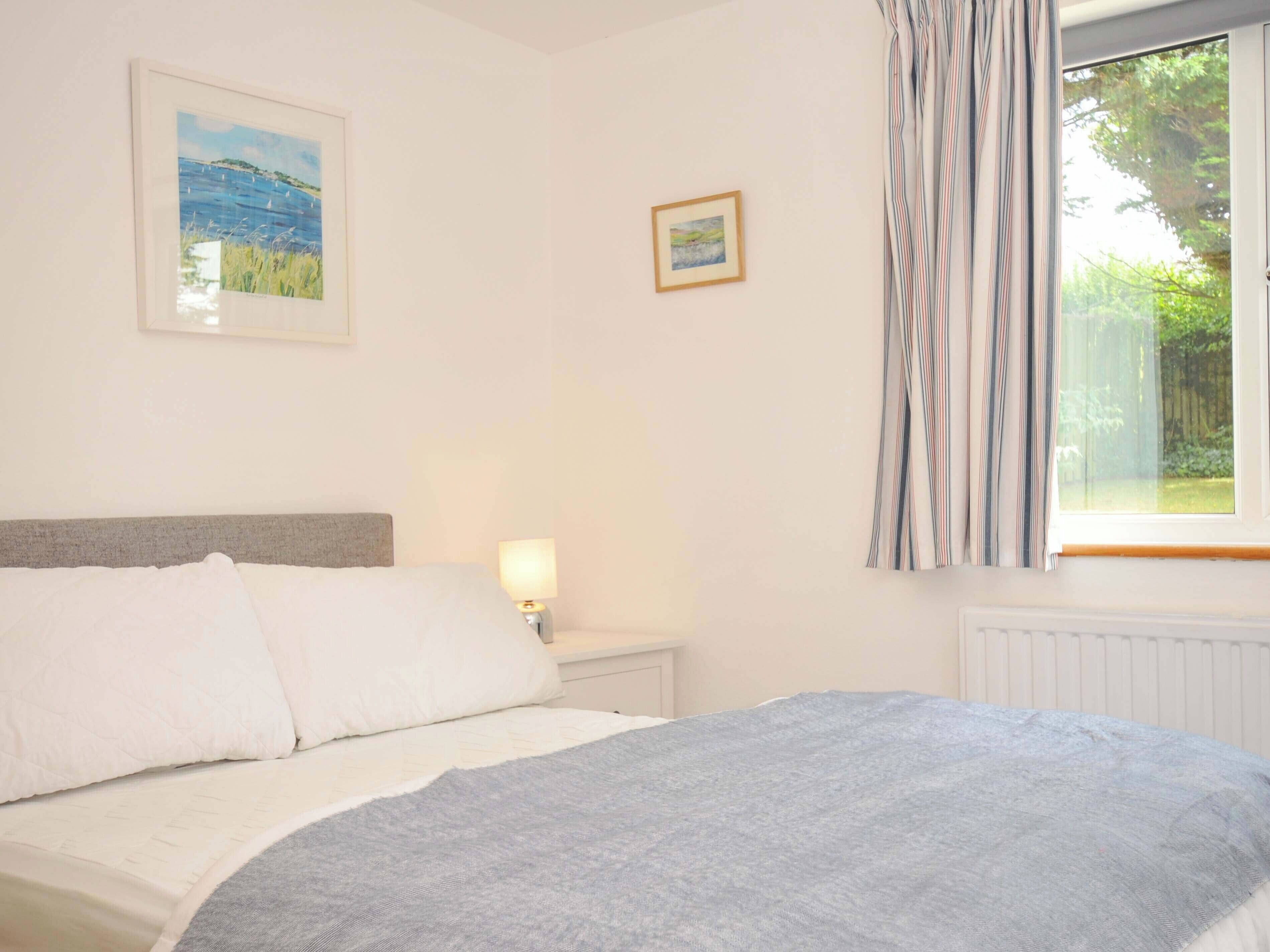 A bedroom with a bed, a nightstand, a lamp, a window with curtains, and two framed pictures on the wall.