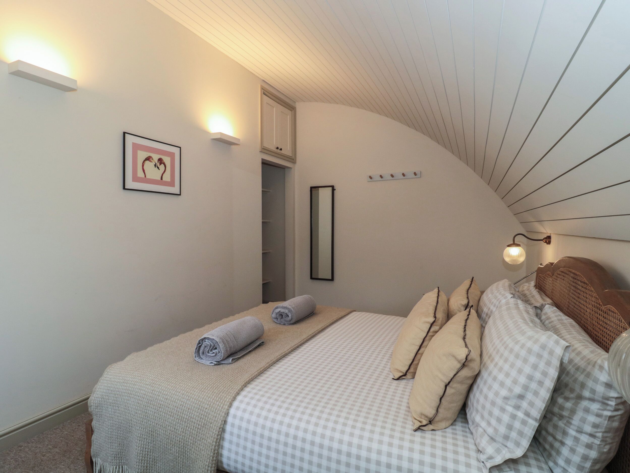 A bedroom with a bed, a framed picture, a mirror, and a light fixture.